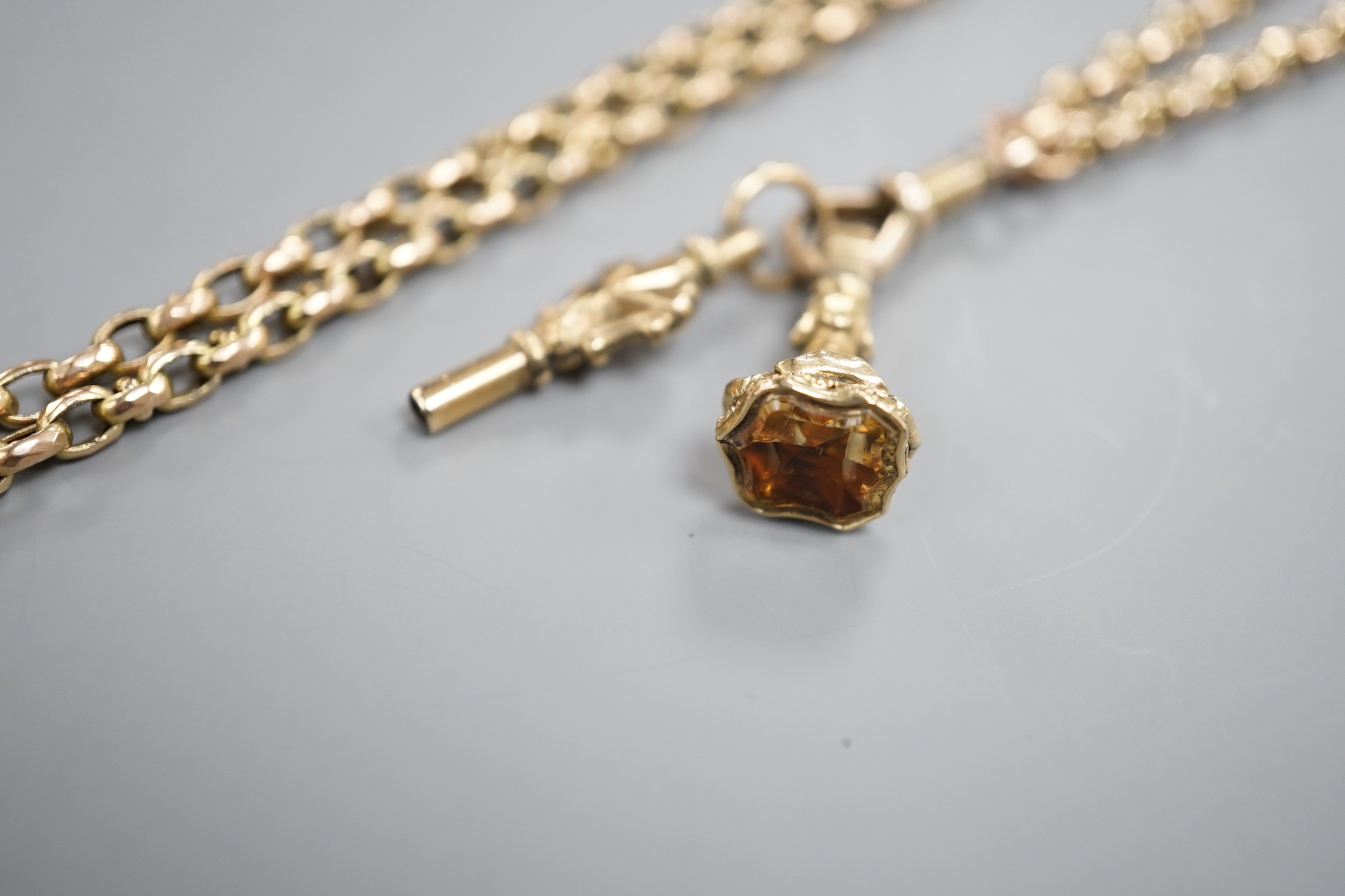 A late Victorian yellow metal guard chain, hung with a watch key and citrine set fob seal, 152cm, gross weight 35.3 grams.